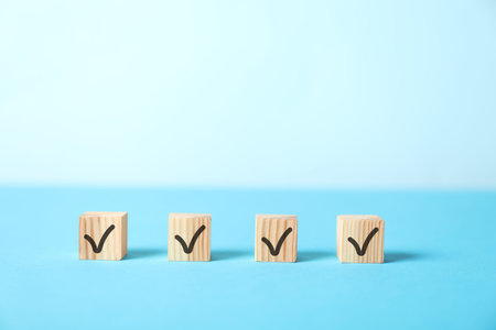Wooden cubes with check marks on light blue background, space for text