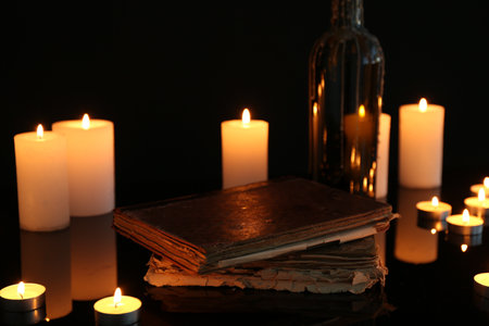 Many burning candles and books on mirror surface against black backgroundの写真素材