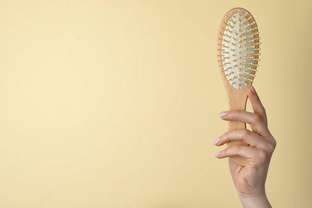 Woman with wooden brush on beige background, closeup. Space for textの写真素材