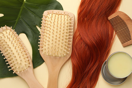 Wooden brushes, wax, comb, lock of hair and monstera leaf on beige background, flat layの写真素材