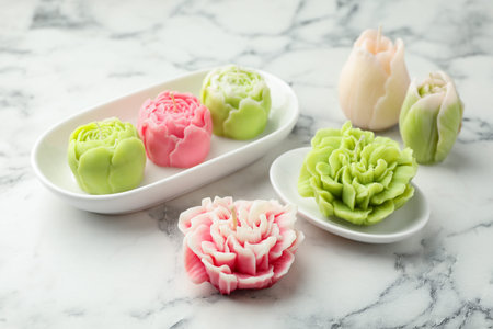 Beautiful flower shaped candles on white marble background, closeup