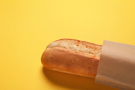 Paper bag with fresh baguette on yellow background, closeup. Space for textの写真素材