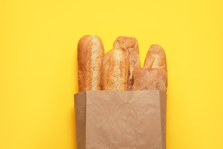 Paper bag with fresh baguettes and ciabatta on yellow background, top viewの写真素材