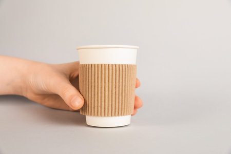 Woman holding paper cup on gray background, closeup. Mockup for design