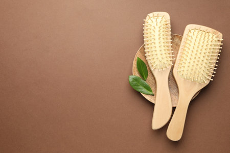 Wooden hair brushes and green leaves on dark beige background, top view. Space for textの写真素材
