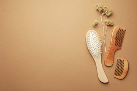 Wooden hair brush, combs and dried flowers on beige background, flat lay. Space for text