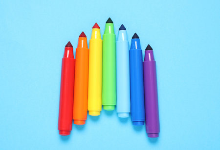 Many colorful markers on light blue background, flat lay