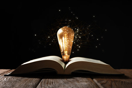 Book with glowing light bulb on wooden table and magic lightsの写真素材