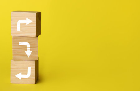 Wooden cubes with arrows pointing in different directions on yellow background, space for text