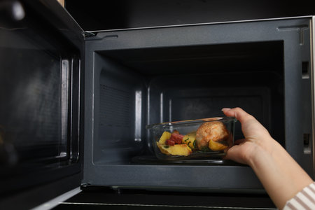 Woman putting container with lunch into microwave indoors, closeupの写真素材
