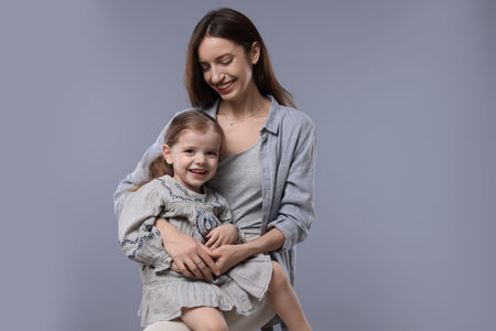 Happy mother with her cute little daughter on grey background