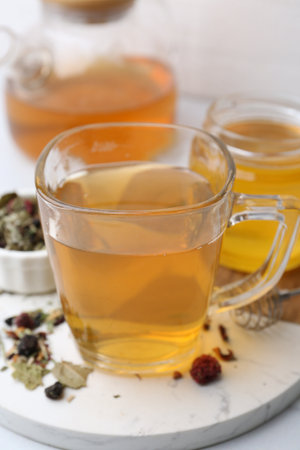 Delicious herbal tea with honey and dry leaves on white table, closeupの写真素材