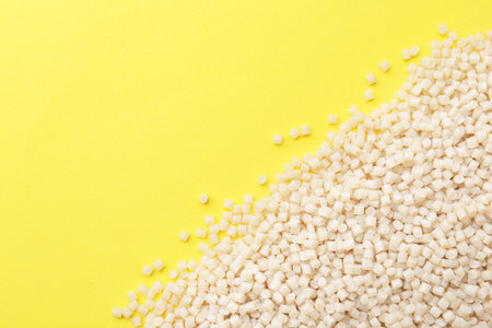 Pile of plastic granules on yellow background, top view. Space for textの写真素材