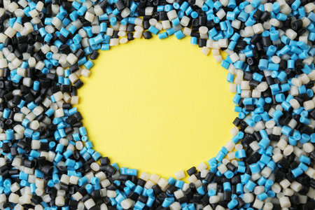 Frame of colorful plastic granules on yellow background, top view. Space for text