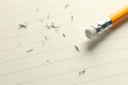 Pencil with eraser and scraps on white sheet of paper, closeup