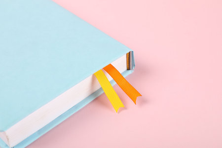 Book with ribbon bookmarks on pink background, closeup. Space for textの写真素材