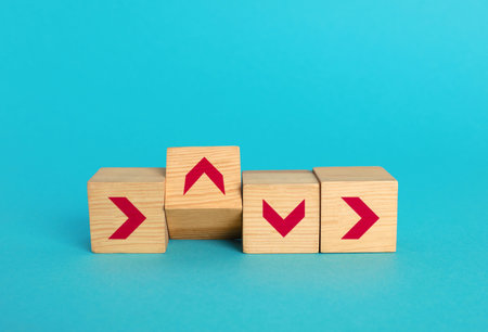 Wooden cubes with arrows pointing in different directions on light blue background