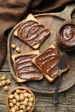 Tasty sandwiches with chocolate butter and hazelnuts on wooden table, flat lay