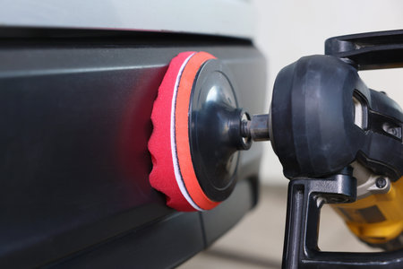 Man polishing car with orbital polisher indoors, closeup
