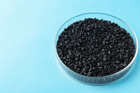 Black plastic granules in petri dish on light blue background, closeup. Space for textの写真素材