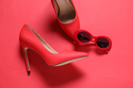 High heeled shoes and sunglasses on crimson background, flat layの写真素材