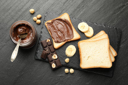 Sandwich with chocolate butter, banana and hazelnuts on black table, flat layの写真素材