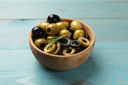 Different delicious marinated olive rings and rosemary in bowl on light blue wooden table, closeupの写真素材