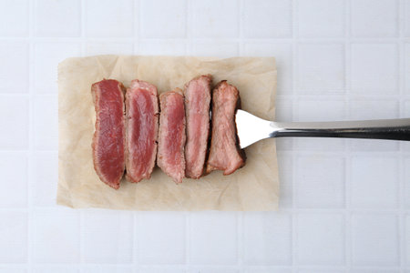 Sliced beef tenderloin with different degrees of doneness on light tiled table, top viewの写真素材