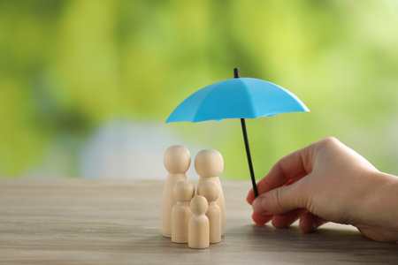 Woman holding umbrella over human figures at wooden table outdoors, closeup. Insurance conceptの写真素材