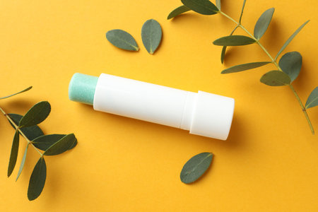 Lip balm and eucalyptus leaves on yellow background, flat lay