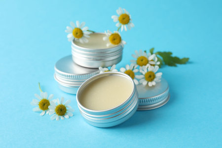 Lip balms and chamomile flowers on light blue background, closeup
