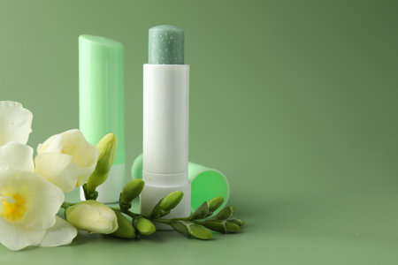 Lip balms and freesia flowers on light green background, closeup. Space for textの写真素材