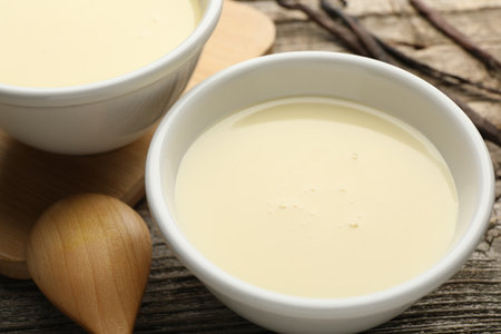 Tasty condensed milk, spoon and vanilla pods on wooden table, closeupの写真素材