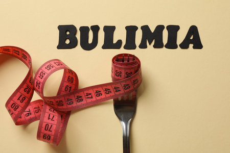 Word Bulimia, fork and measuring tape on beige background, top viewの写真素材
