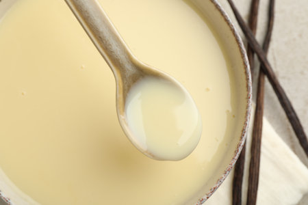 Taking tasty vanilla condensed milk with spoon from bowl on light grey table, flat layの写真素材