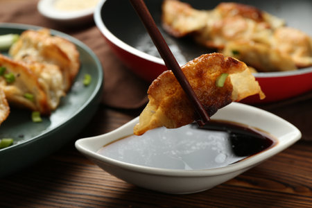 Dipping tasty fried gyoza (dumpling) into soy sauce on wooden table, closeupの写真素材