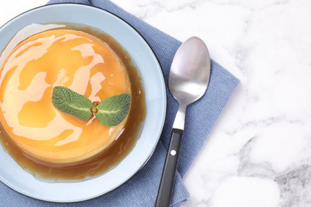 Delicious pudding with caramel sauce and mint on white marble table, top view. Space for textの写真素材