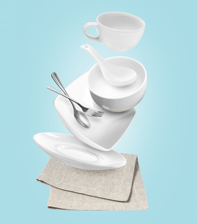 Clean dishware and silverware flying over napkin on light blue backgroundの写真素材