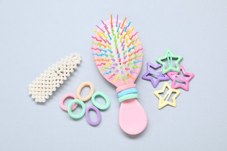 Different hair accessories and brush on grey background, flat lay