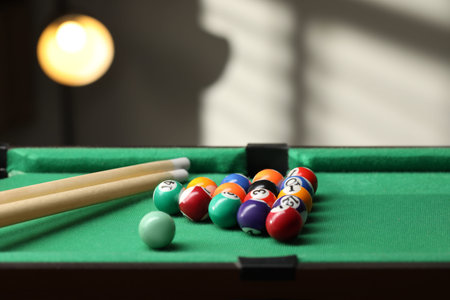 Billiard balls in triangle and cues on green table indoors. Space for text