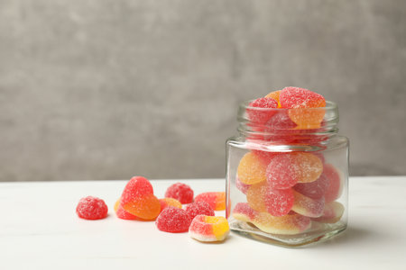 Tasty jelly candies in glass jar on white table against gray background. Space for textの写真素材
