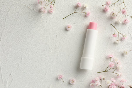 Moisturizing lip balm and gypsophila flowers on light textured table, flat lay. Space for textの写真素材