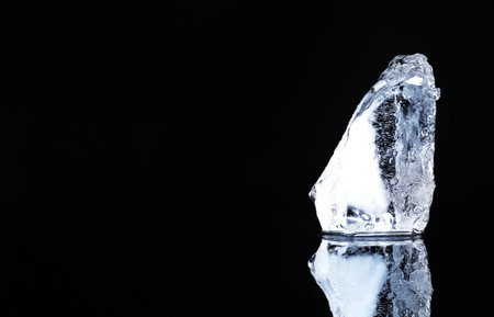 Piece of clear ice on black mirror surface, space for textの写真素材