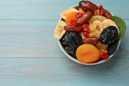 Mix of different dried fruits in bowl on light blue wooden table, top view. Space for textの写真素材