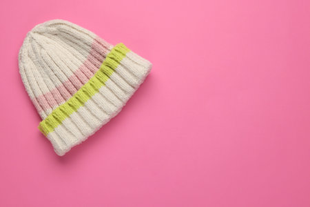 Warm woolen hat on pink background, top view. Space for text