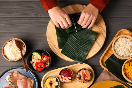 Woman tying banana leaf with food at wooden table with products, top view. Healthy eco servingの写真素材