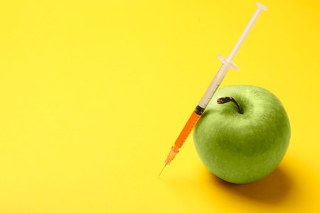 GMO concept. Green apple and syringe with liquid on yellow background, closeup. Space for textの写真素材