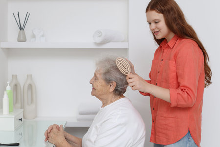 Granddaughter brushing her grandmother with brush at homeの写真素材