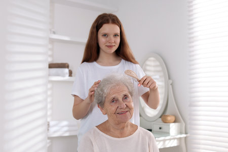 Granddaughter brushing her grandmother with brush at homeの写真素材