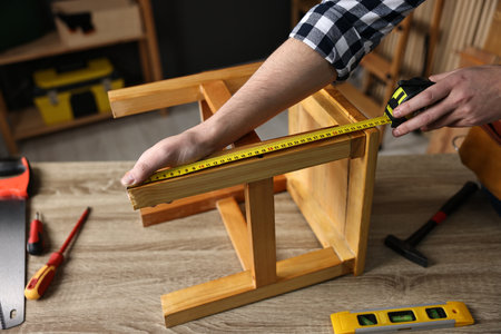 Repairman measuring wooden stool at table in workshop, closeupの写真素材
